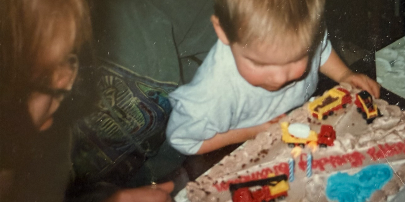 A little boy blows out the candles at his second birthday party as his mom looks on.